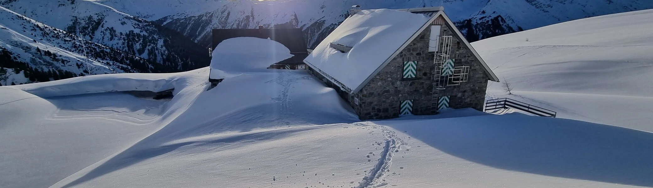 eingeschneite Friedrichshafener Hütte mit Sonne im Hintergrund | © (c) 2024 DAV Friedrichshafen - R. Klees