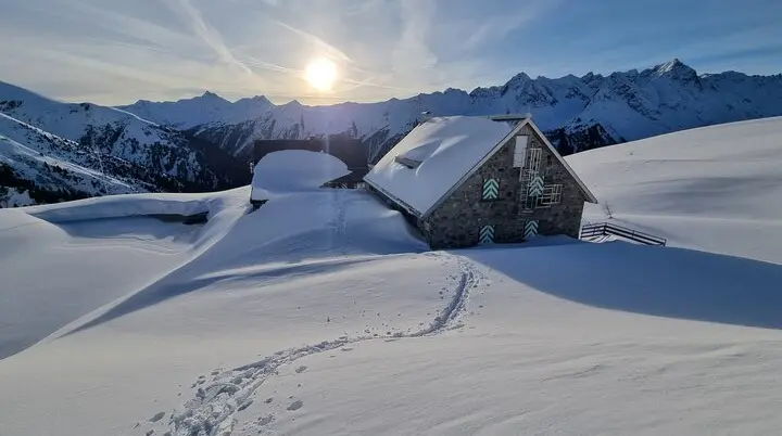 eingeschneite Friedrichshafener Hütte mit Sonne im Hintergrund | © (c) 2024 DAV Friedrichshafen - R. Klees