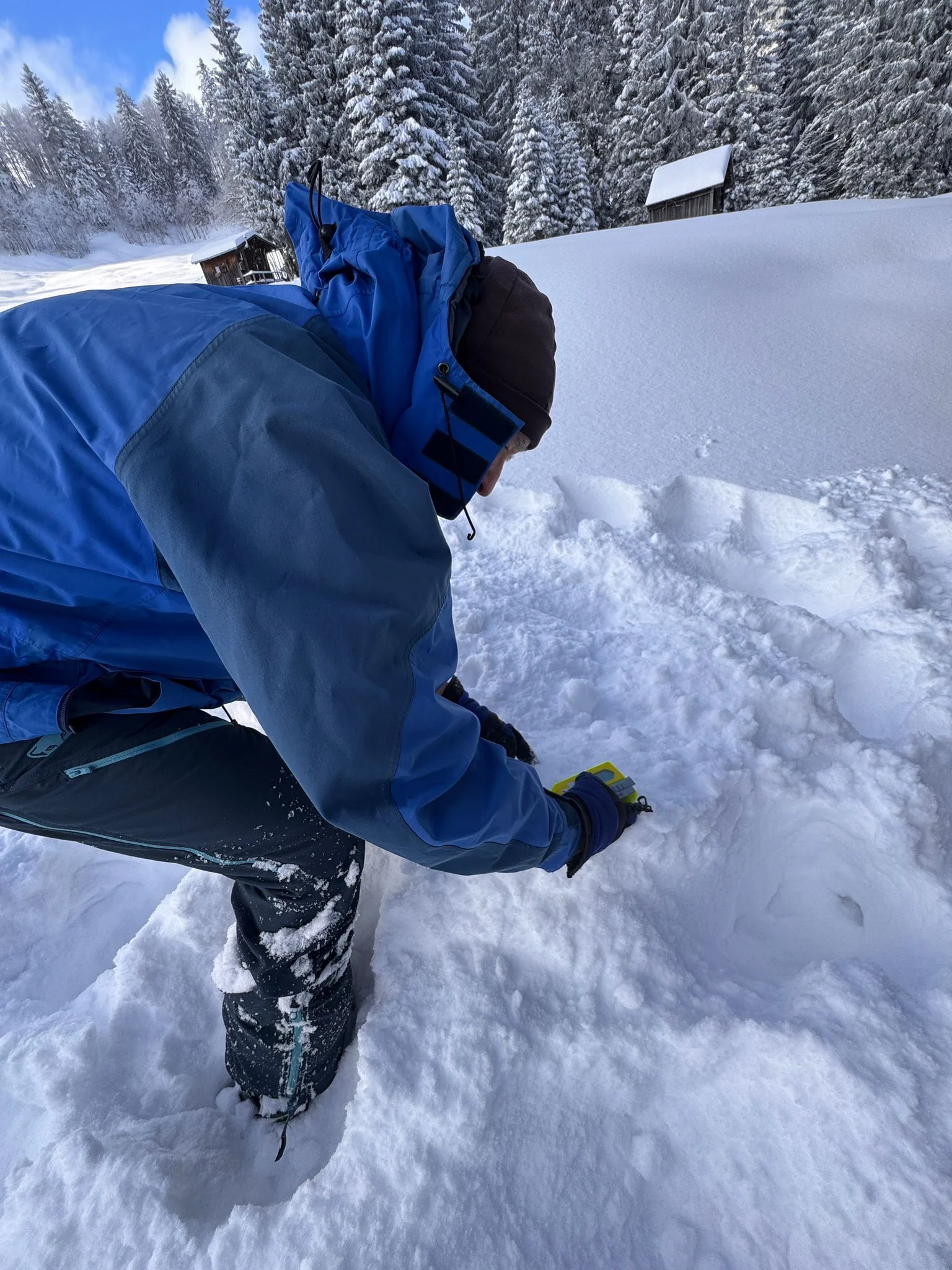 Person in blauer Winterjacke und schwarzer Mütze kniet im Schnee und übt die Feinsuche mit dem LVS-Gerät | © DAV-FN / Th. Gläser