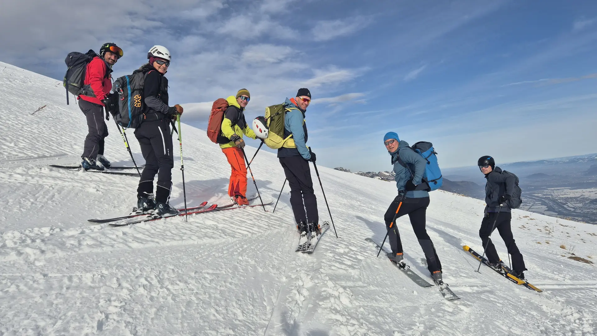 Sechs Skifahrer in bunter Ausrüstung stehen auf schneebedecktem Hang unter blauem Himmel | © DAV-Fn / R. Lebedeff