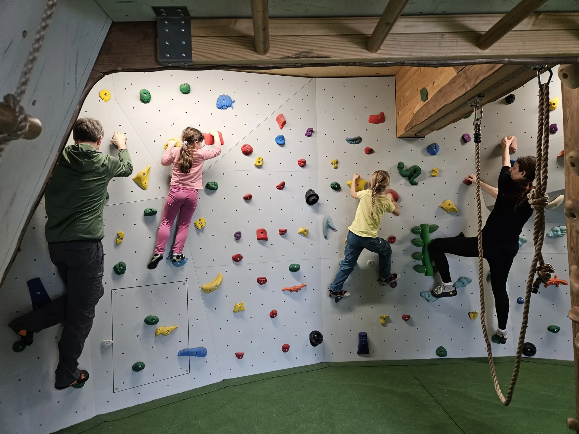 Vier Kinder klettern an einer Kletterwand mit bunten Griffen in einem Raum mit Holzbalken | © DAV-FN / A. Schababerle