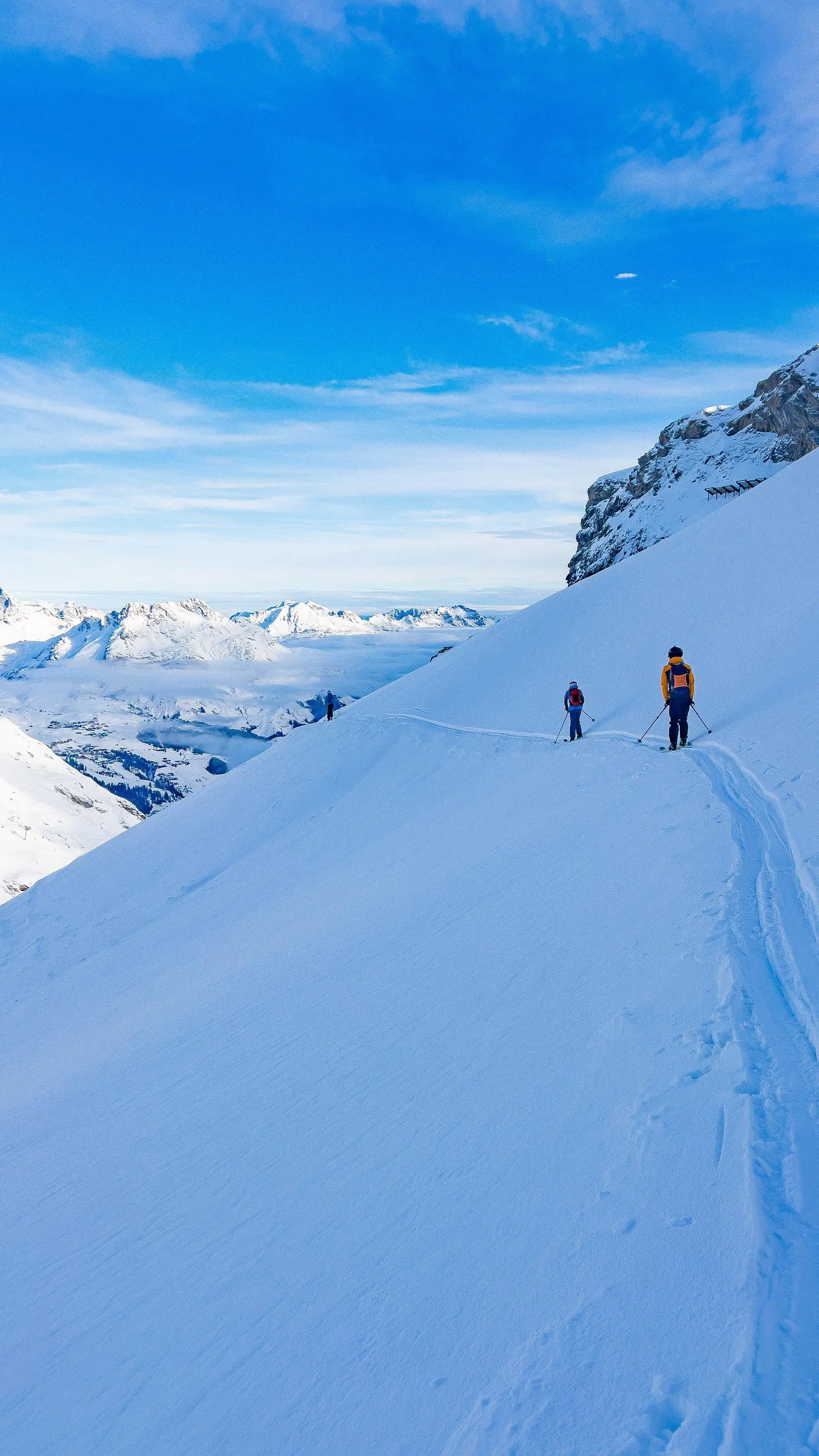 Zwei Skifahrer auf einer schneebedeckten Bergpiste mit Bergpanorama und blauem Himmel | © DAV-FN / S. Schmidhuber