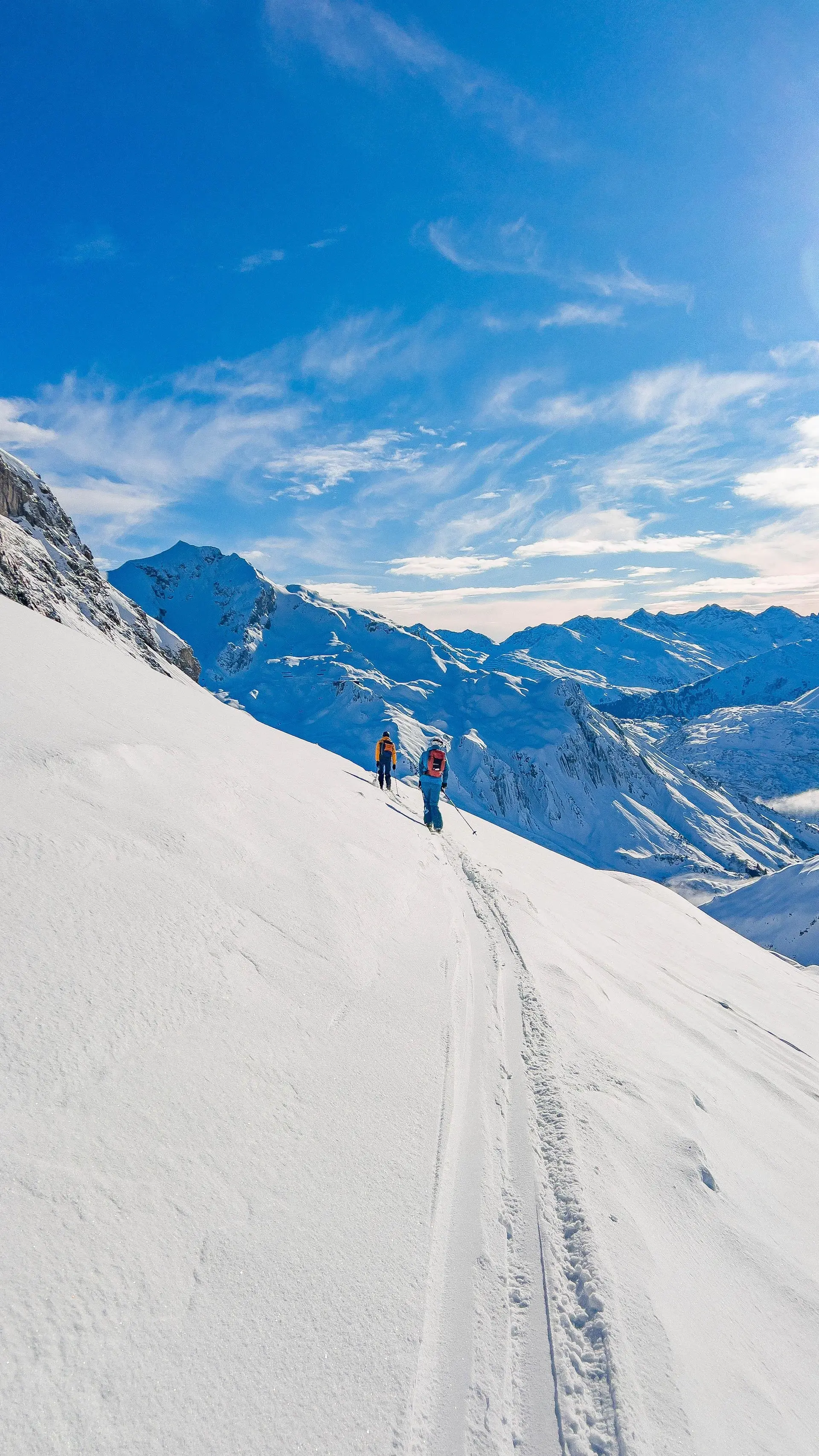 Zwei Personen mit Rucksäcken wandern auf einer schneebedeckten Bergflanke unter blauem Himmel | © DAV-FN / S. Schmidhuber