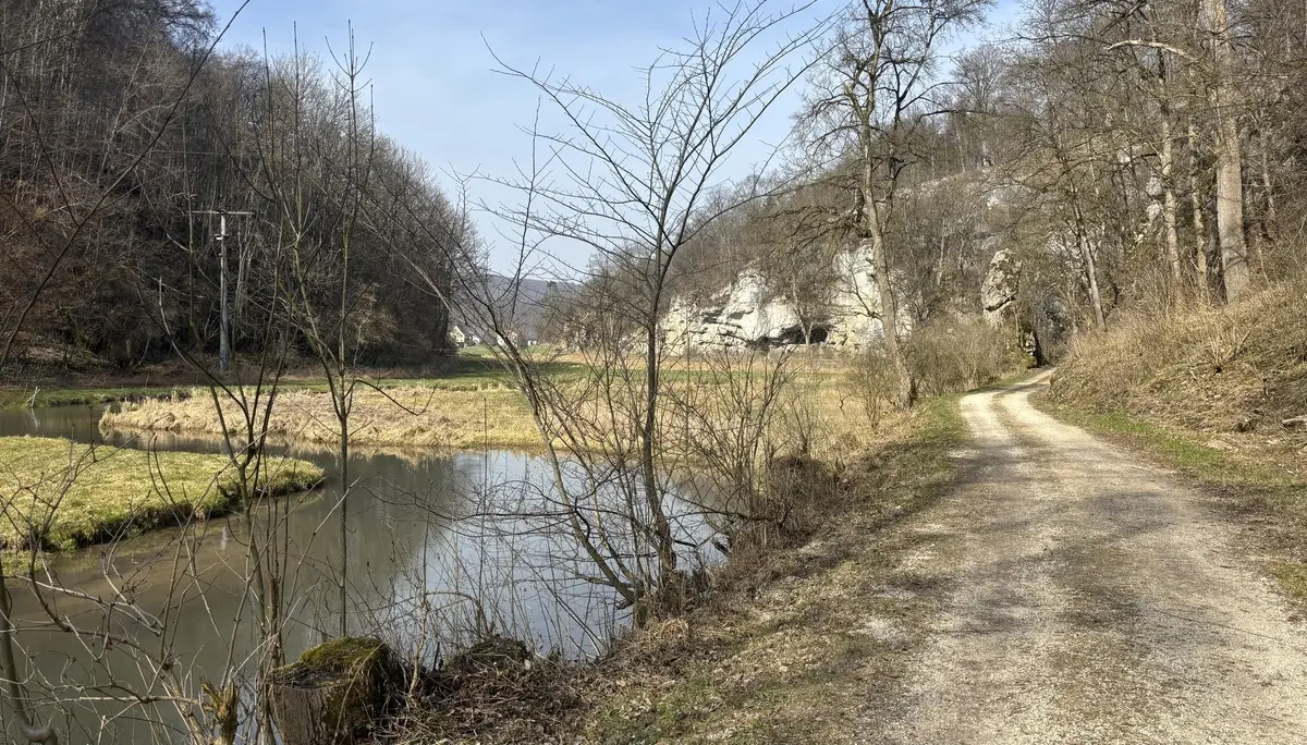 Wanderweg entlang eines ruhigen Flusses mit kahlen Bäumen und Felsen im Hintergrund | © DAV-FN / A. Schech