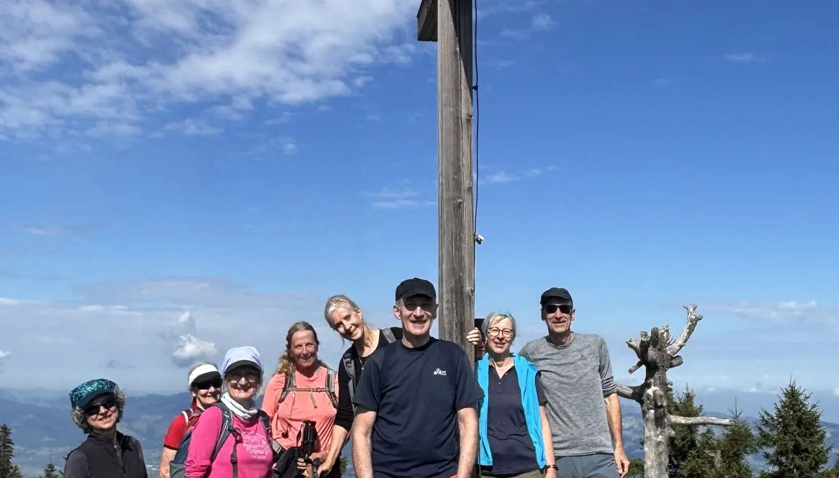 Gruppe von acht Wanderern steht auf einer Bergwiese vor einem großen Holzkreuz unter blauem Himmel mit Wolken | © DAV-FN / A, Schech