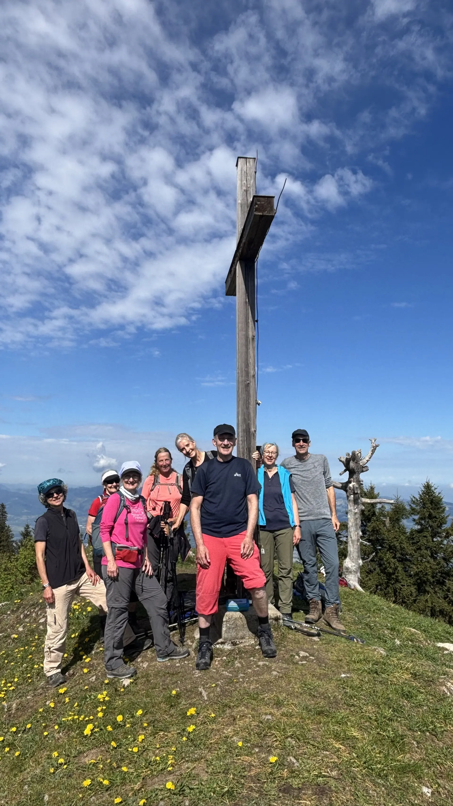 Gruppe von acht Wanderern steht auf einer Bergwiese vor einem großen Holzkreuz unter blauem Himmel mit Wolken | © DAV-FN / A, Schech