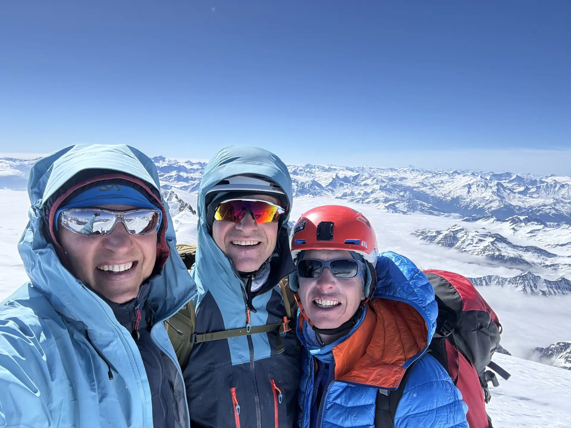 Drei Personen in Winterjacken und Helmen stehen auf einem schneebedeckten Berg mit Bergpanorama im Hintergrund | © DAV-FN / R. Gersten