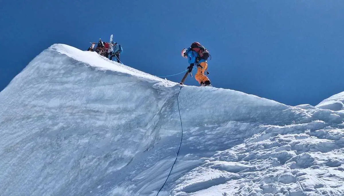 Bergsteiger in orangefarbener Hose sichert sich mit Seil auf schneebedecktem Grat unter blauem Himmel | © DAV-FN / R. Gersten