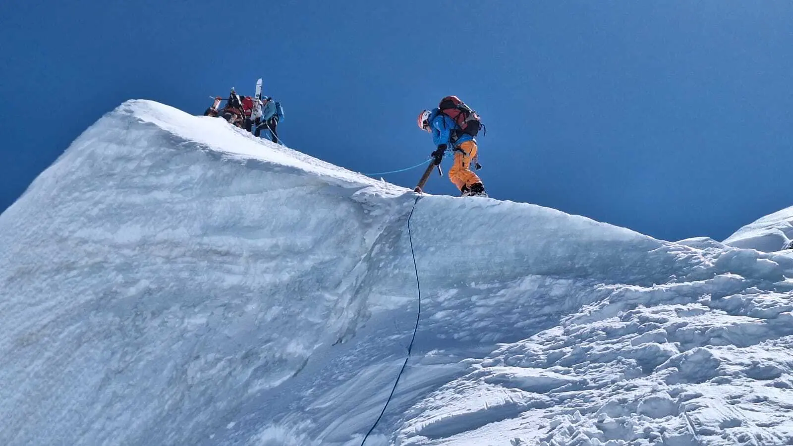 Bergsteiger in orangefarbener Hose sichert sich mit Seil auf schneebedecktem Grat unter blauem Himmel | © DAV-FN / R. Gersten
