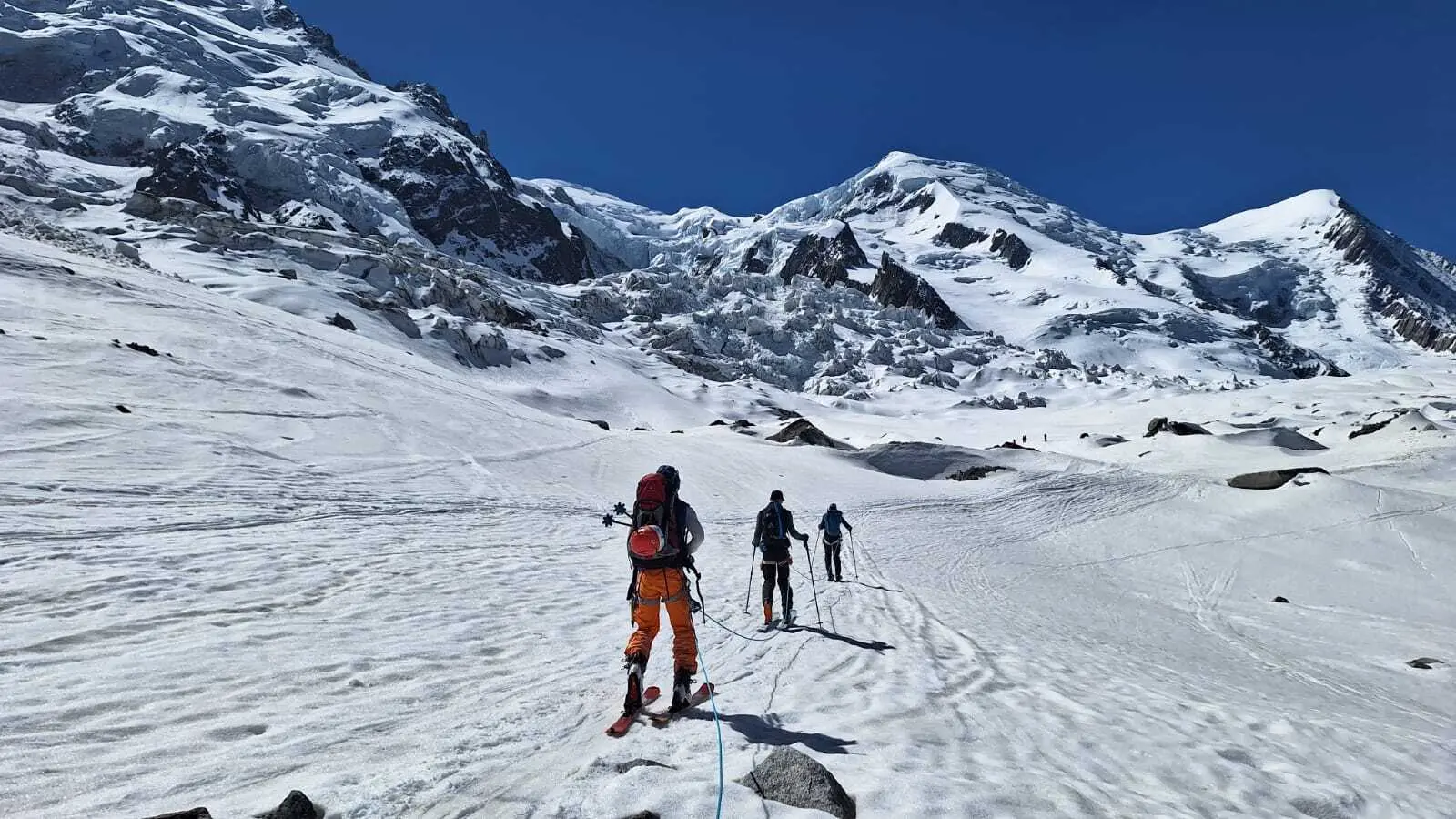 Drei Skifahrer mit Rucksäcken steigen eine schneebedeckte Berglandschaft mit steilen Gipfeln im Hintergrund hinauf | © DAV-FN / R. Gersten