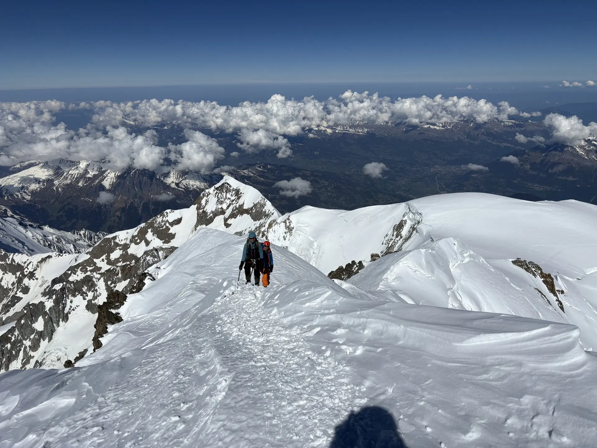 Zwei Personen wandern auf einem schneebedeckten Berggrat unter blauem Himmel mit Wolken und Bergpanorama im Hintergrund | © DAV-FN / R. Gersten
