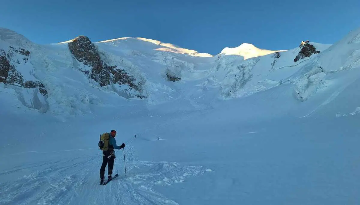 Person mit Rucksack und Wanderstöcken auf schneebedecktem Berghang unter blauem Himmel | © DAV-FN / R. Gersten