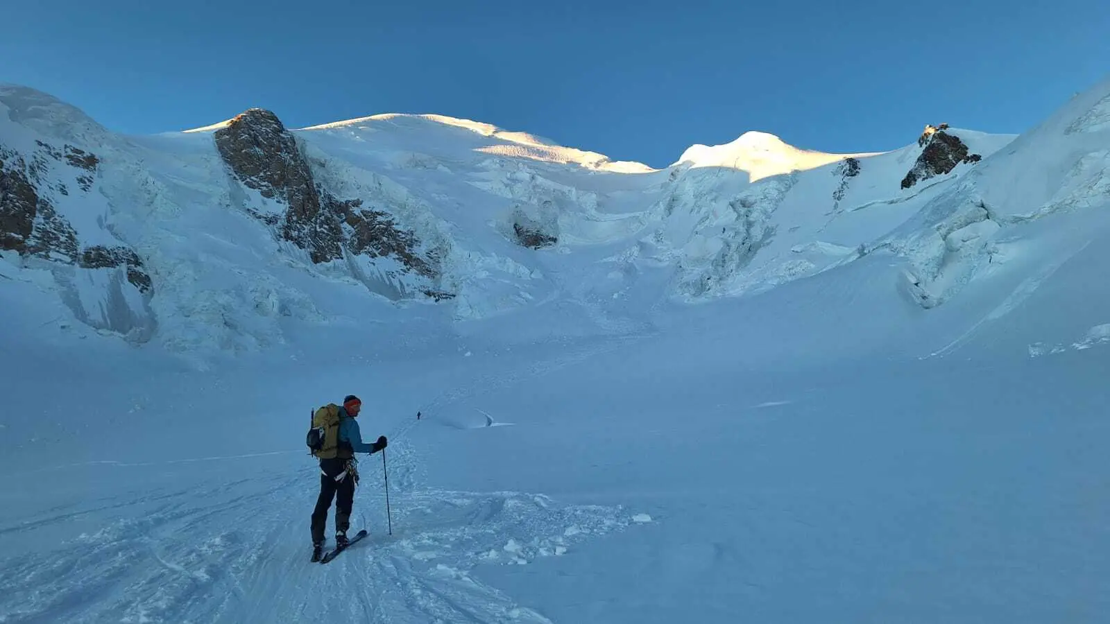 Person mit Rucksack und Wanderstöcken auf schneebedecktem Berghang unter blauem Himmel | © DAV-FN / R. Gersten