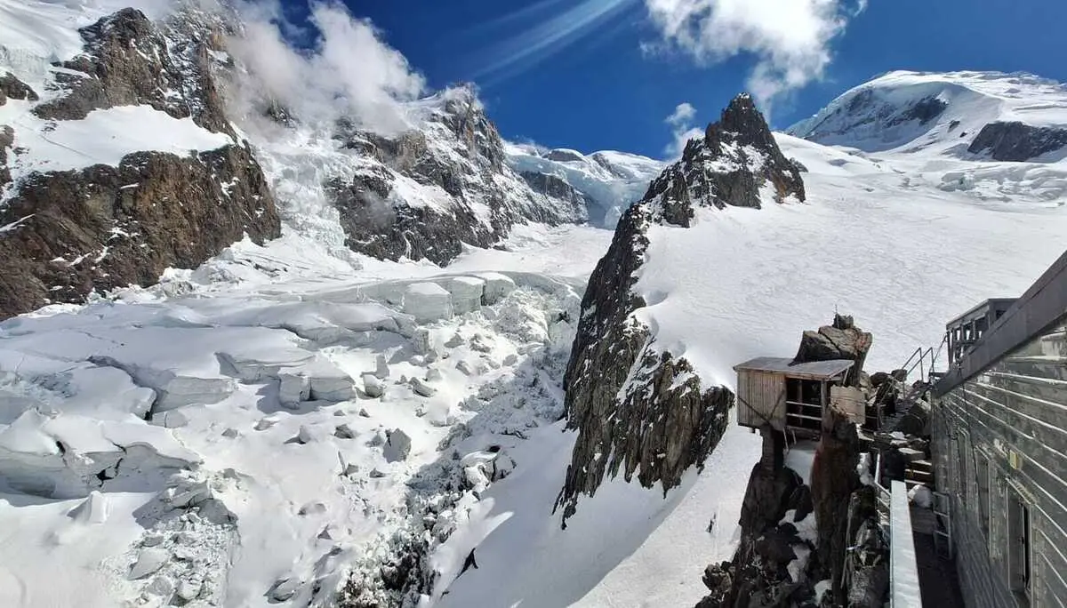 Berglandschaft mit schneebedeckten Gipfeln, Gletscher und einer Berghütte auf einem Felsen unter blauem Himmel mit Wolken | © DAV-FN / R. Gersten