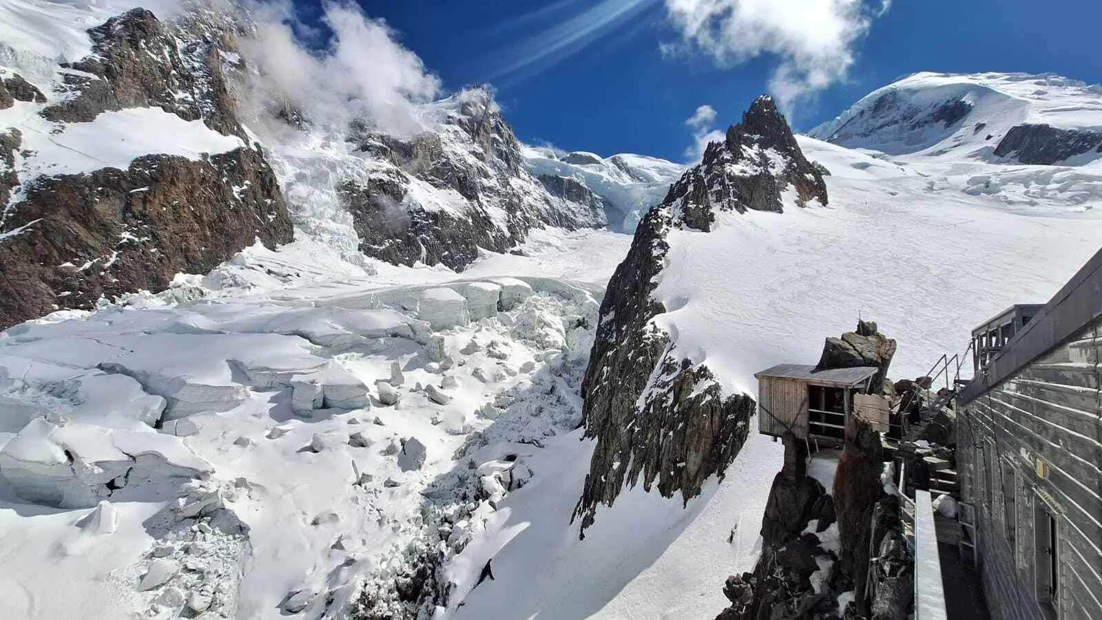 Berglandschaft mit schneebedeckten Gipfeln, Gletscher und einer Berghütte auf einem Felsen unter blauem Himmel mit Wolken | © DAV-FN / R. Gersten