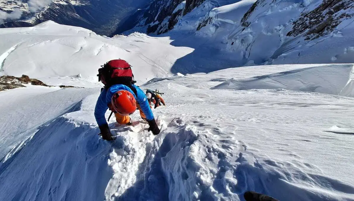 Bergsteiger mit rotem Helm und blauem Oberteil klettert steilen schneebedeckten Hang hinab | © DAV-FN / R. Gersten
