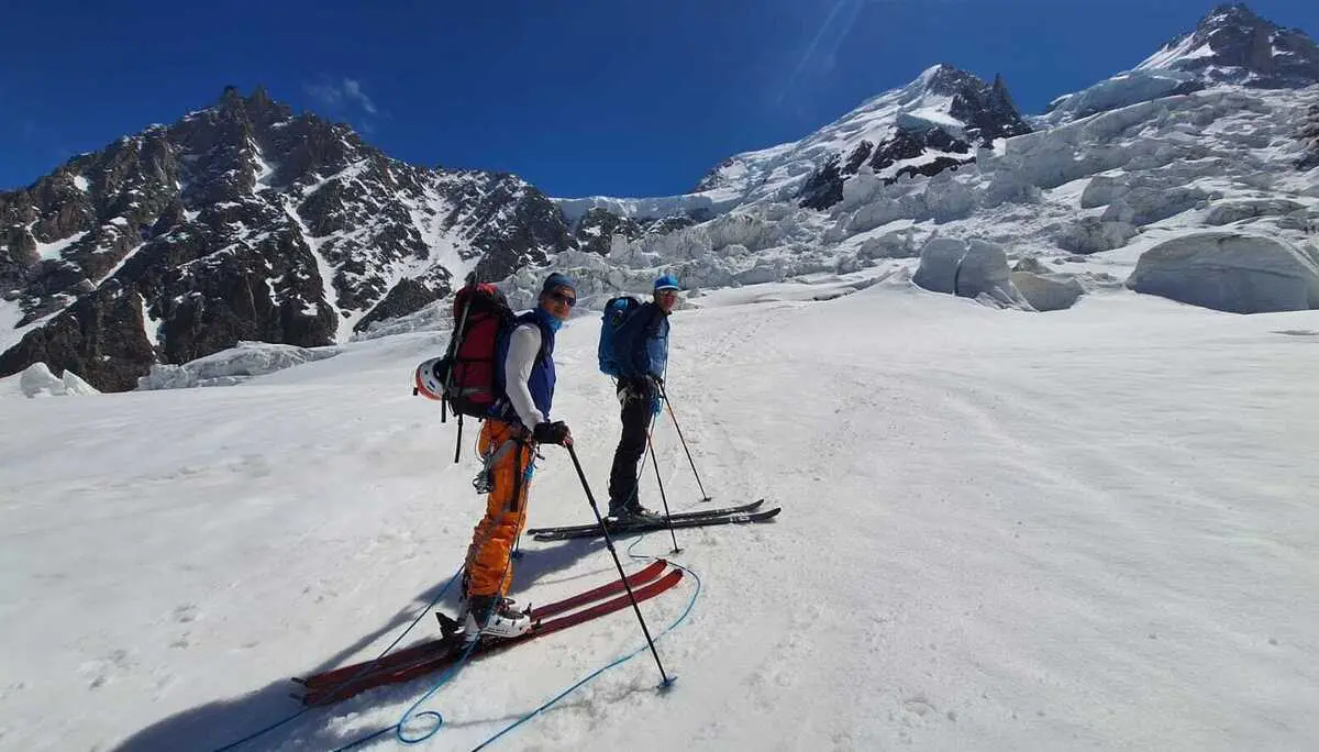 Zwei Skifahrer mit Rucksäcken stehen auf schneebedecktem Hang vor schroffen Berggipfeln | © DAV-FN / R. Gersten