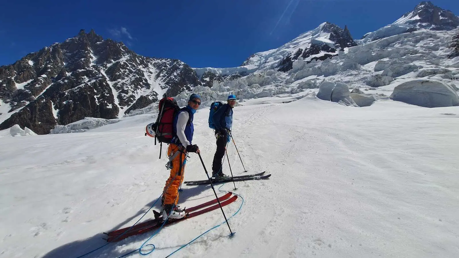Zwei Skifahrer mit Rucksäcken stehen auf schneebedecktem Hang vor schroffen Berggipfeln | © DAV-FN / R. Gersten