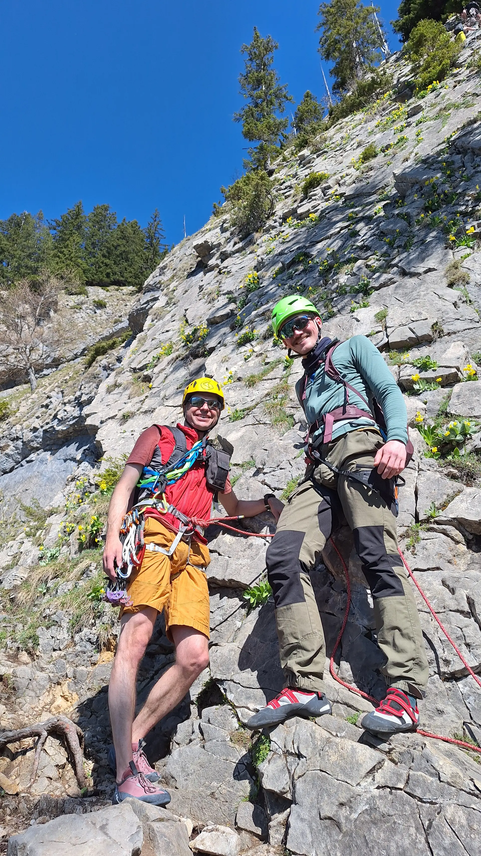 Zwei Männer mit Kletterausrüstung stehen an einem Felsen unter blauem Himmel | © DAV-FN / R. Huber