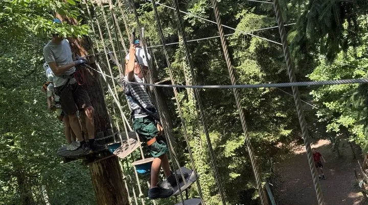 Zwei Personen mit Kletterausrüstung balancieren auf einem Hochseilgarten-Parcours zwischen Bäumen | © DAV-FN / A. Schababerle