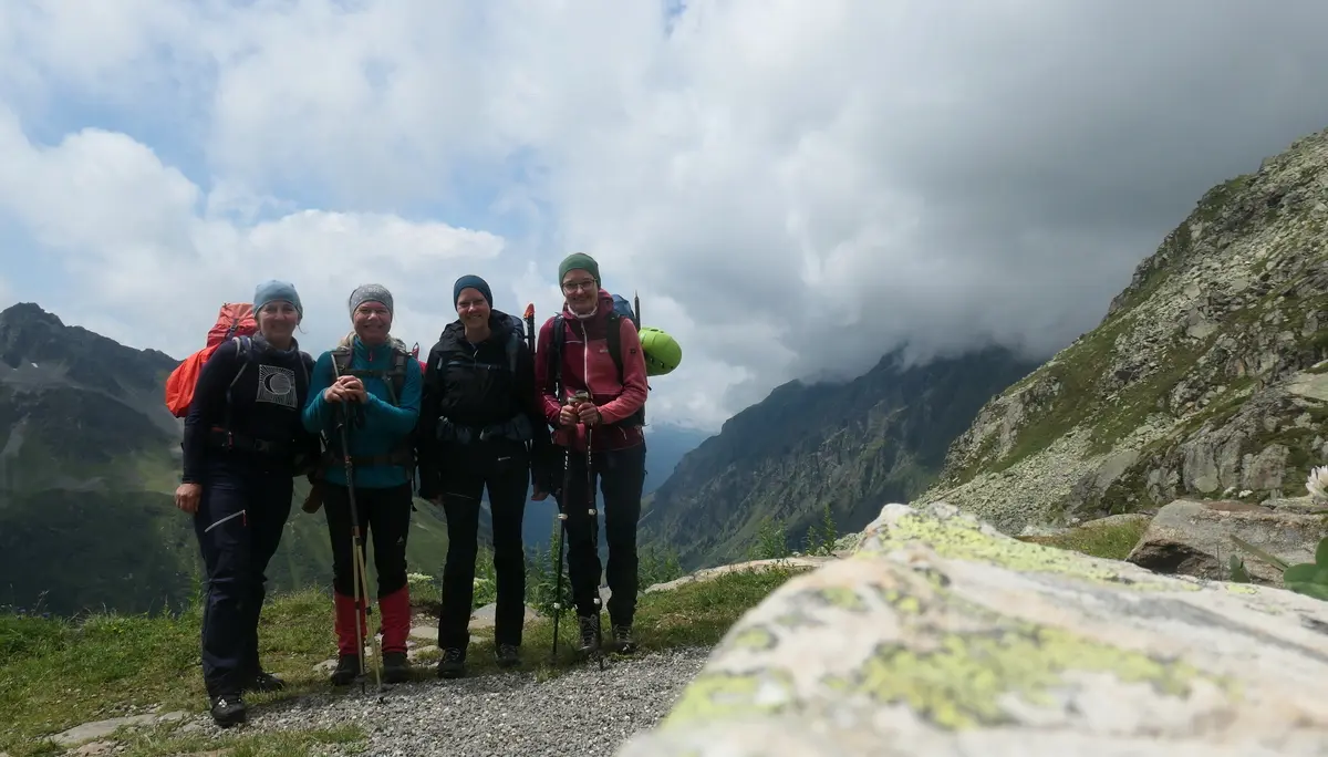 Vier Wanderer mit Rucksäcken und Wanderstöcken stehen auf einem Bergpfad vor bewölktem Himmel und Berggipfeln | © DAV - FN / S. Dischler