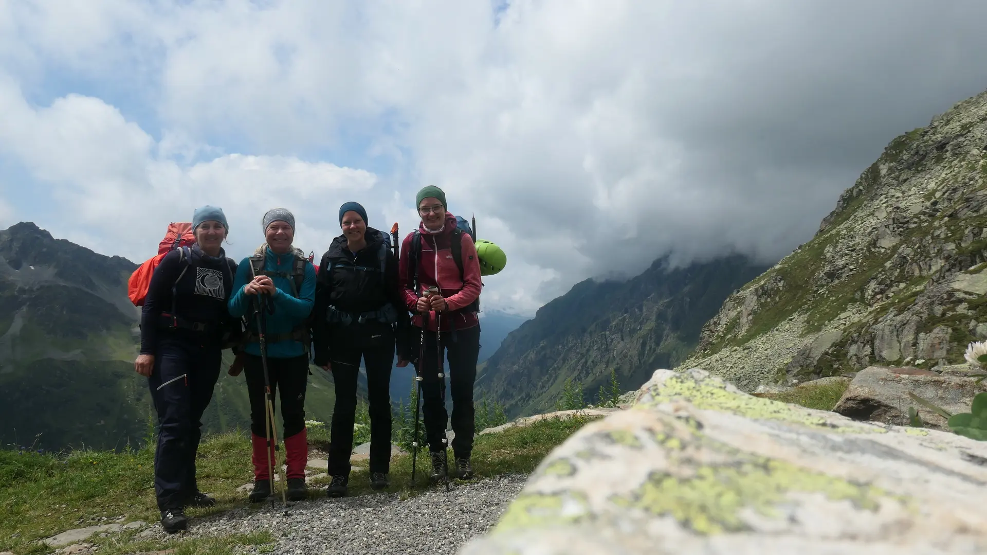Vier Wanderer mit Rucksäcken und Wanderstöcken stehen auf einem Bergpfad vor bewölktem Himmel und Berggipfeln | © DAV - FN / S. Dischler