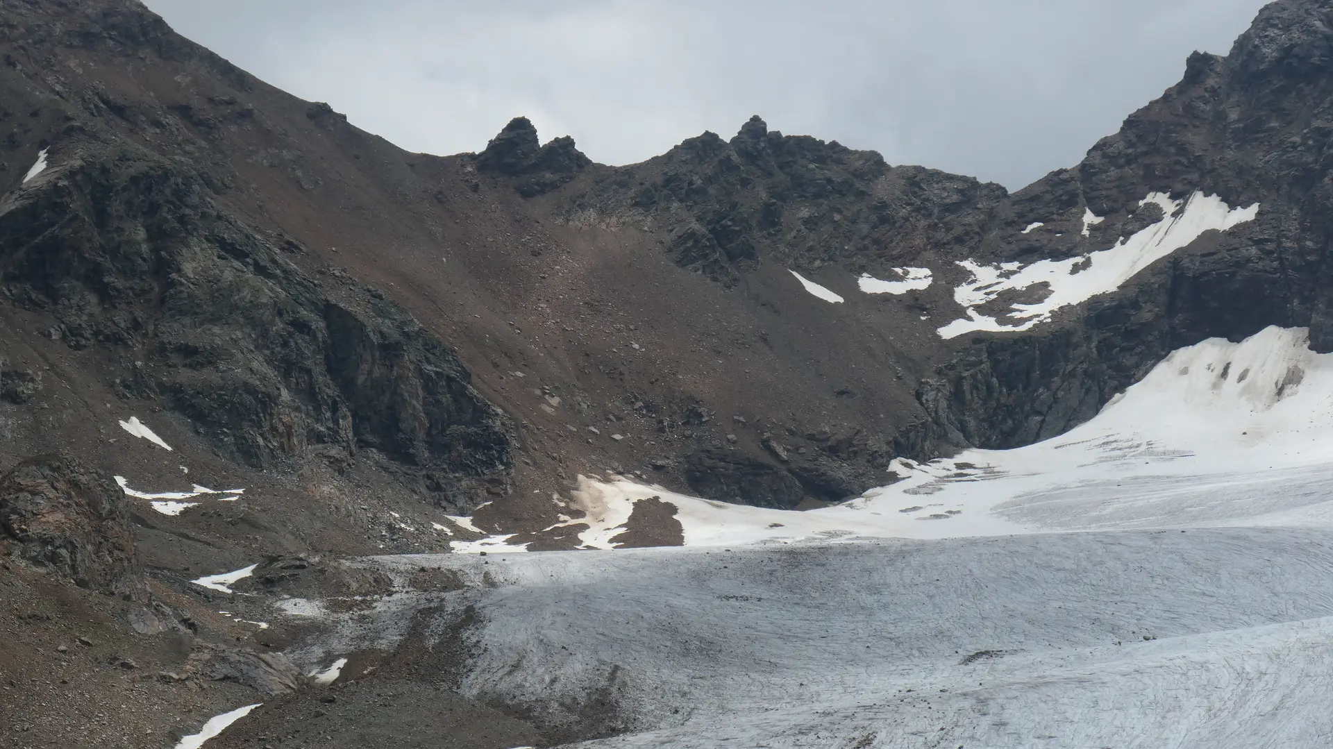Gletscher mit Schnee- und Eisflächen vor felsigen Berggipfeln unter bewölktem Himmel | © DAV - FN / S. Dischler