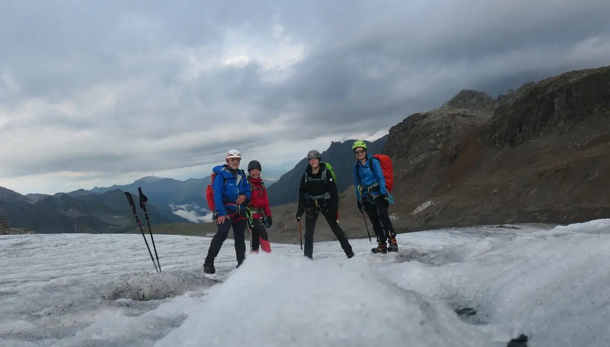 Vier Bergsteiger mit Rucksäcken und Helmen stehen auf einem Gletscher vor bewölktem Himmel und Berglandschaft | © DAV - FN / S. Dischler