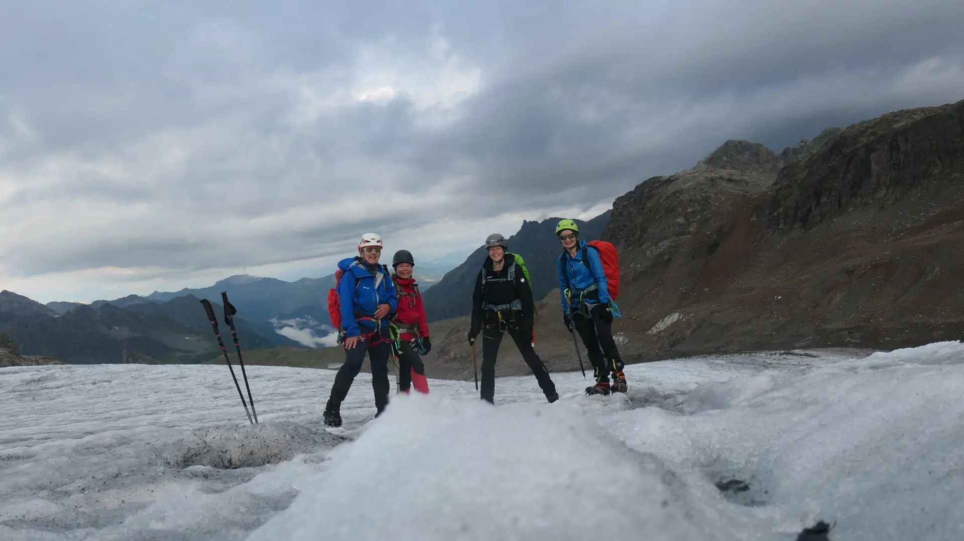 Vier Bergsteiger mit Rucksäcken und Helmen stehen auf einem Gletscher vor bewölktem Himmel und Berglandschaft | © DAV - FN / S. Dischler
