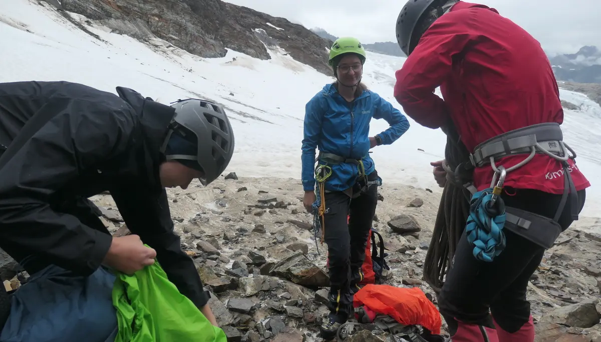 Drei Bergsteiger mit Helmen und Kletterausrüstung stehen auf felsigem Boden vor schneebedecktem Berg | © DAV - FN / S. Dischler