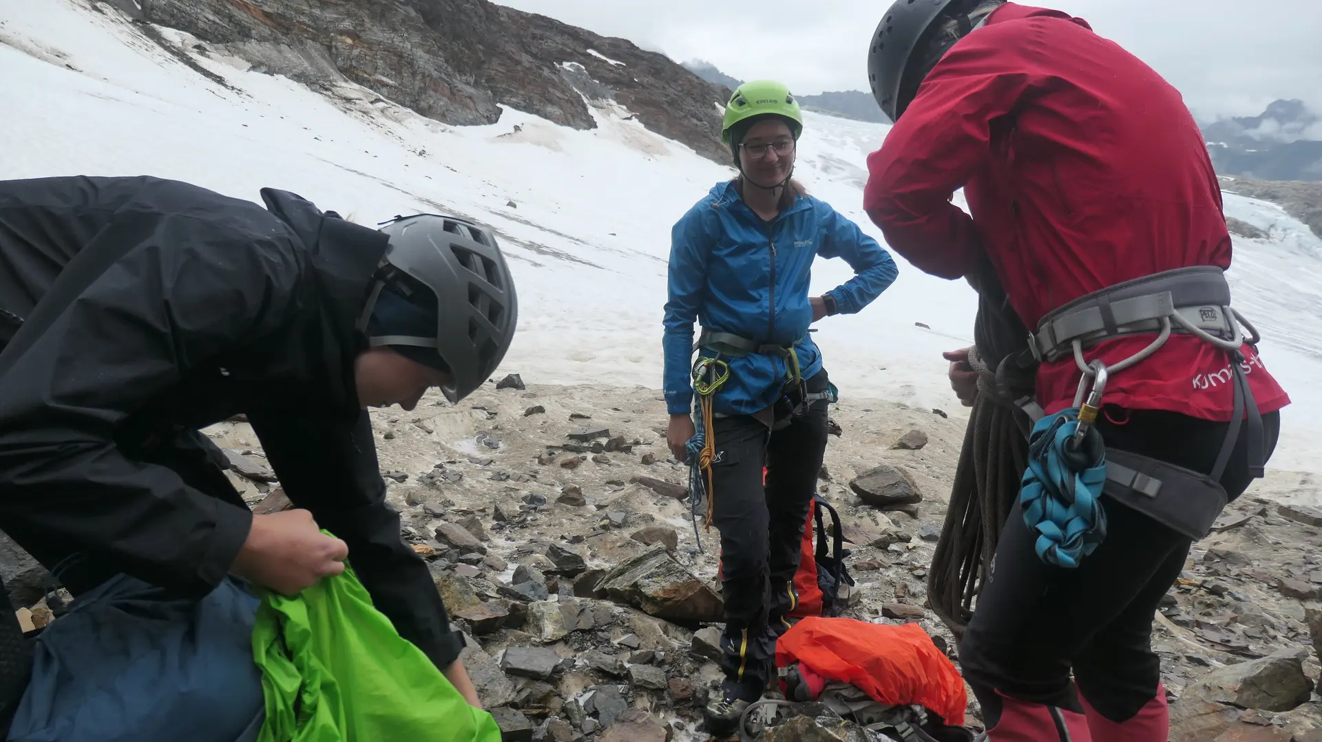 Drei Bergsteiger mit Helmen und Kletterausrüstung stehen auf felsigem Boden vor schneebedecktem Berg | © DAV - FN / S. Dischler