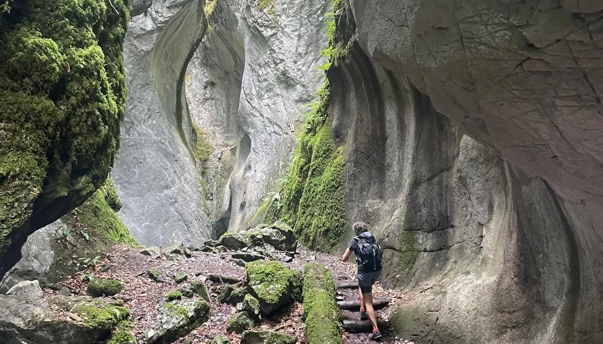 Wanderer mit Rucksack auf schmalem Pfad zwischen hohen, moosbewachsenen Felswänden in einer Schlucht | © DAV - FN / K. Seuster