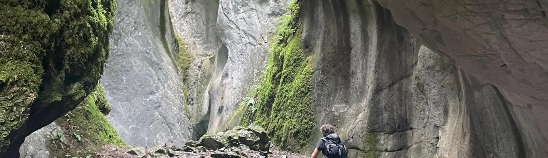 Wanderer mit Rucksack auf schmalem Pfad zwischen hohen, moosbewachsenen Felswänden in einer Schlucht | © DAV - FN / K. Seuster