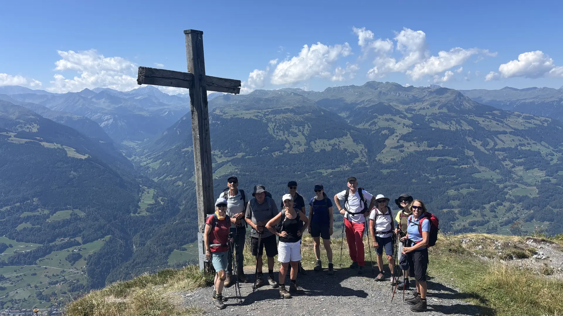 Gruppe von Wanderern steht auf einem Berggipfel neben einem großen Holzkreuz mit Berglandschaft im Hintergrund | © DAV - FN / A. Schech