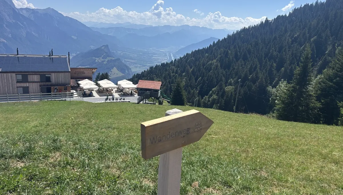 Wegweiser mit der Aufschrift 'Wanderweg' auf einer Wiese vor einem Berghaus und bewaldeten Bergen | © DAV - FN / A. Schech