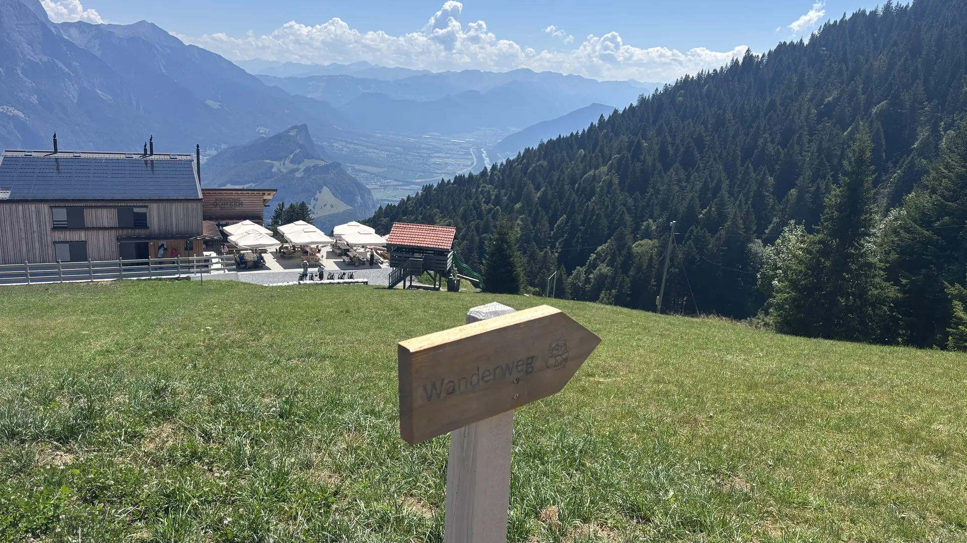 Wegweiser mit der Aufschrift 'Wanderweg' auf einer Wiese vor einem Berghaus und bewaldeten Bergen | © DAV - FN / A. Schech