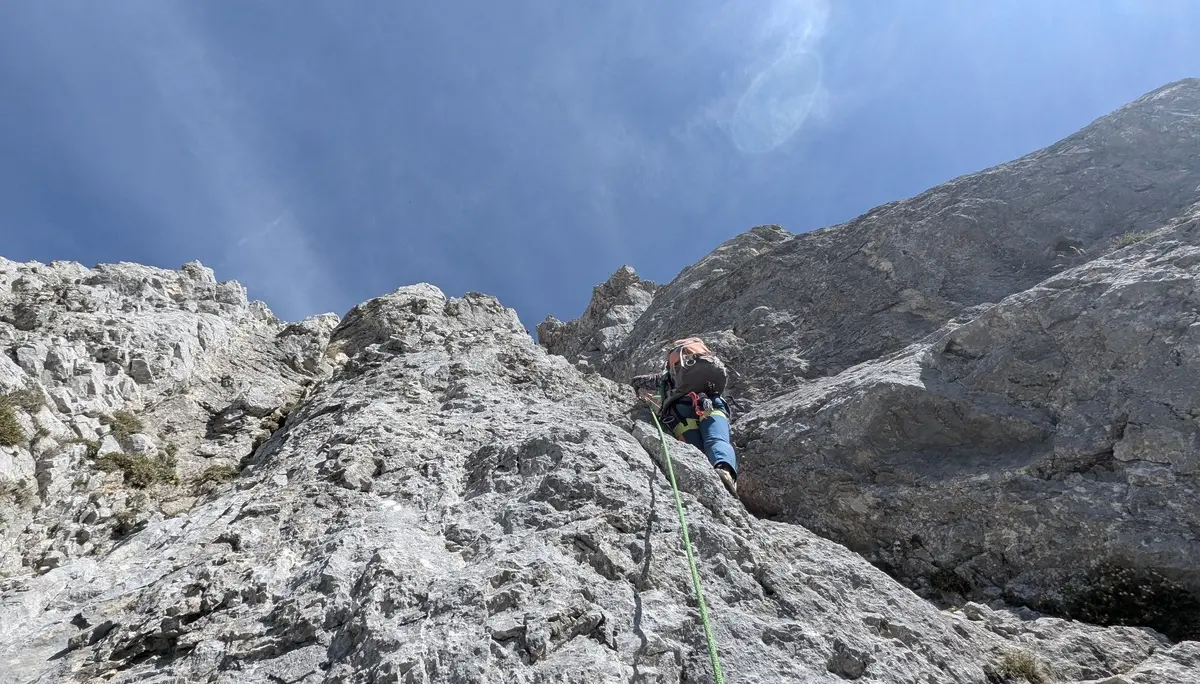 Bergsteiger mit Rucksack und Kletterseil klettert an steiler Felswand unter blauem Himmel | © DAV - FN / Yannic K., Robert H.