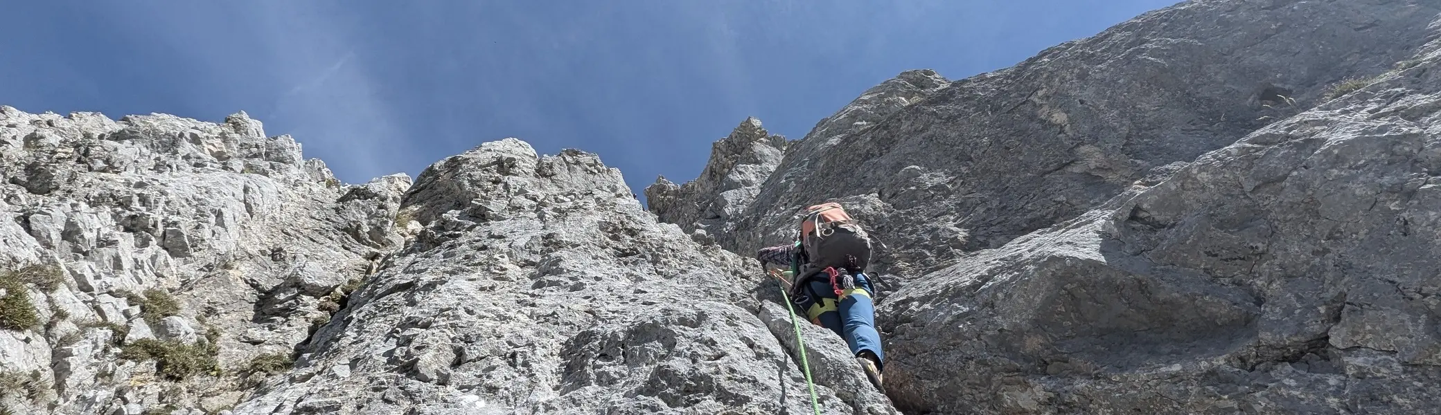 Bergsteiger mit Rucksack und Kletterseil klettert an steiler Felswand unter blauem Himmel | © DAV - FN / Yannic K., Robert H.