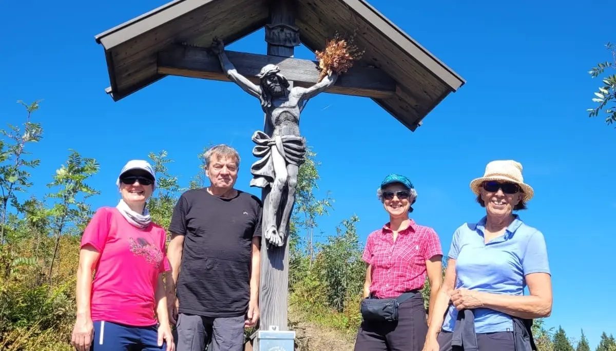 Vier Wanderer stehen neben einem hölzernen Kreuz mit einer Jesusfigur unter blauem Himmel | © DAV - FN / A. Sahovic
