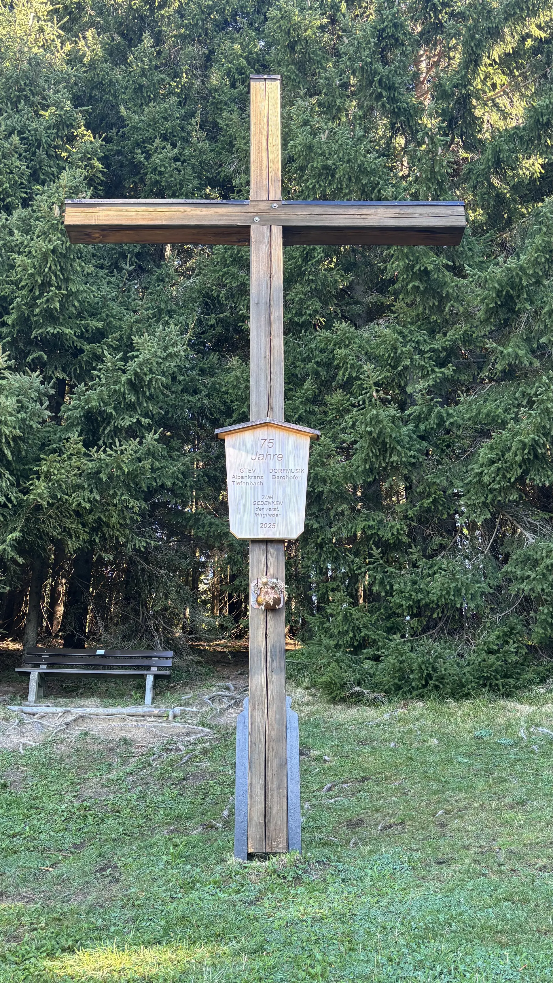 Holzkreuz mit einem Schild und einem Kranz vor einem Wald und einer Bank | © DAV - FN / A. Schech