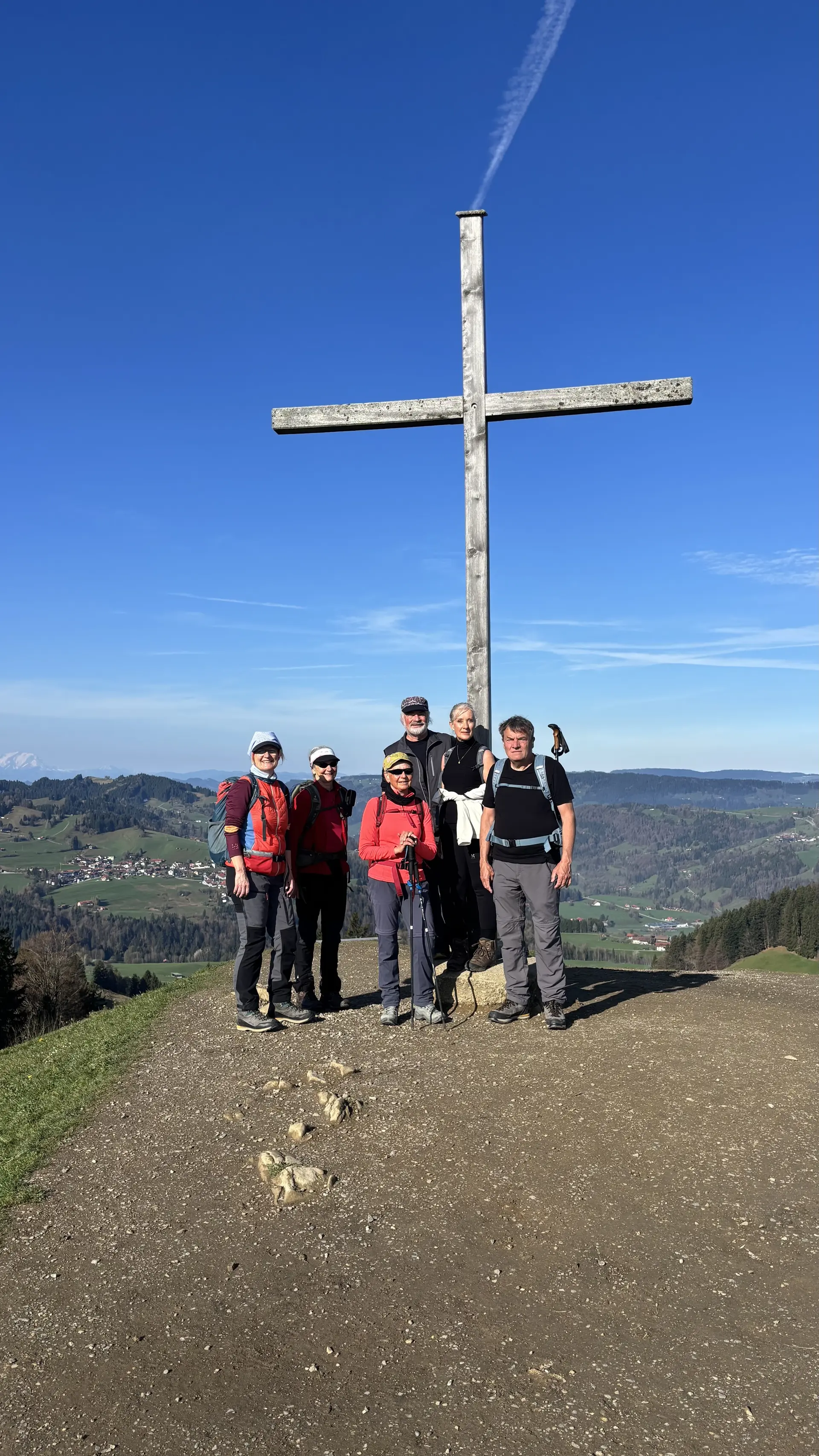 Sechs Wanderer stehen vor einem großen Holzkreuz auf dem Hündlekopf mit Blick auf eine ländliche Landschaft unter blauem Himmel | © DAV-FN / A. Schech