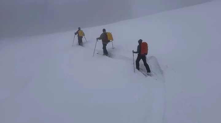 Drei Skitourengeher mit Rucksäcken und Skistöcken steigen in nebliger Winterlandschaft einen schneebedeckten Hang hinauf | © DAV-FN / Th. Gläser
