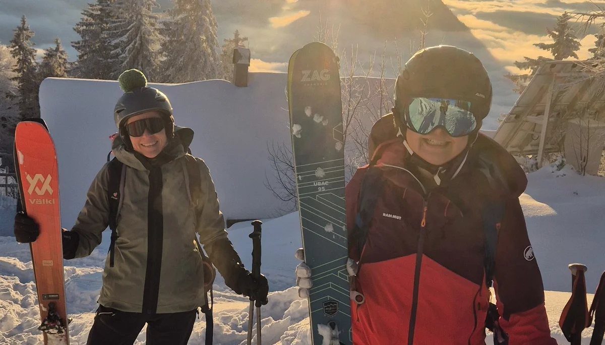 Zwei Personen mit Skiern und Skistöcken stehen auf schneebedecktem Berggipfel bei Sonnenuntergang mit Bergpanorama im Hintergrund | © DAV-FN / R. Lebedeff