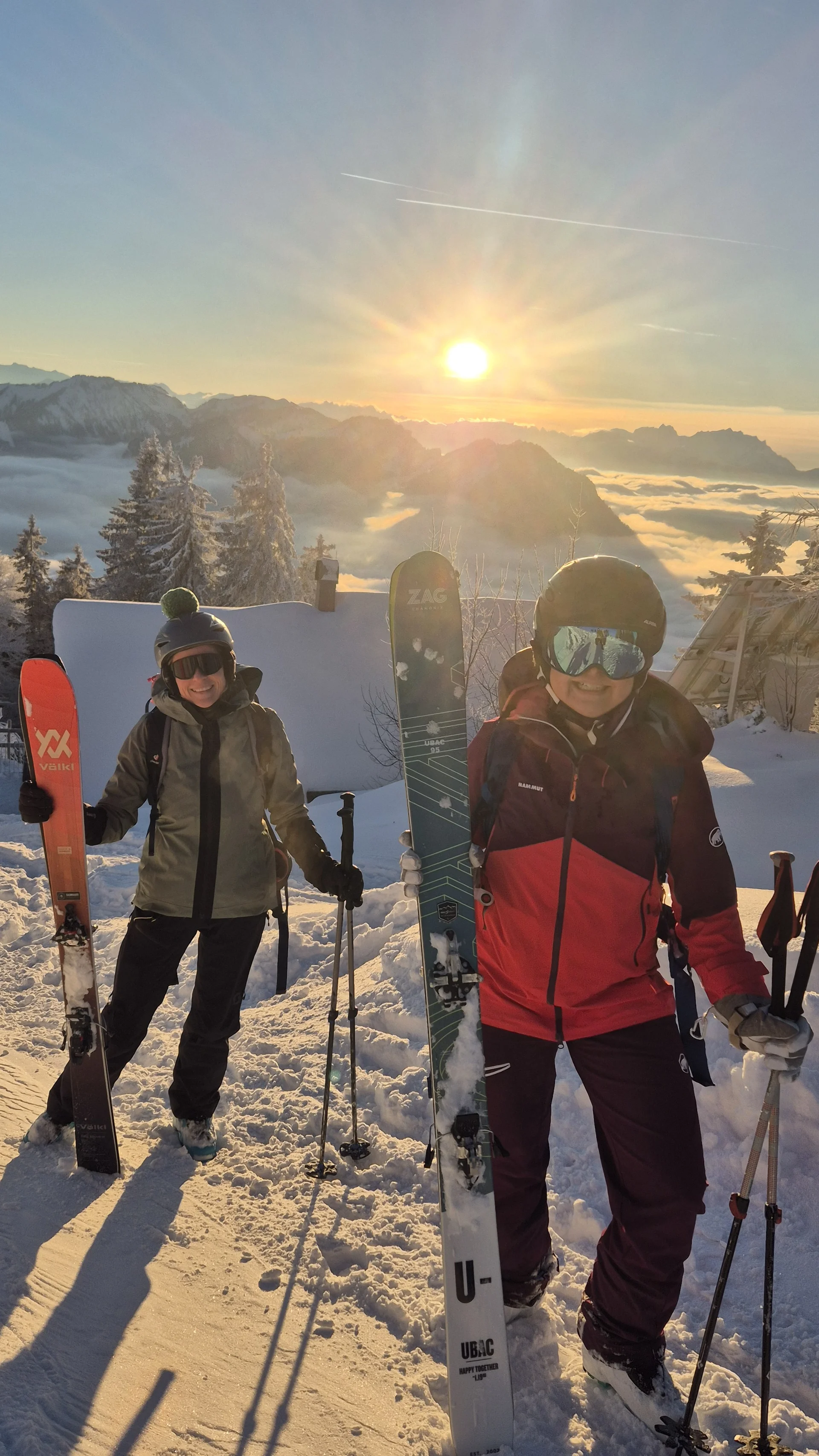 Zwei Personen mit Skiern und Skistöcken stehen auf schneebedecktem Berggipfel bei Sonnenuntergang mit Bergpanorama im Hintergrund | © DAV-FN / R. Lebedeff