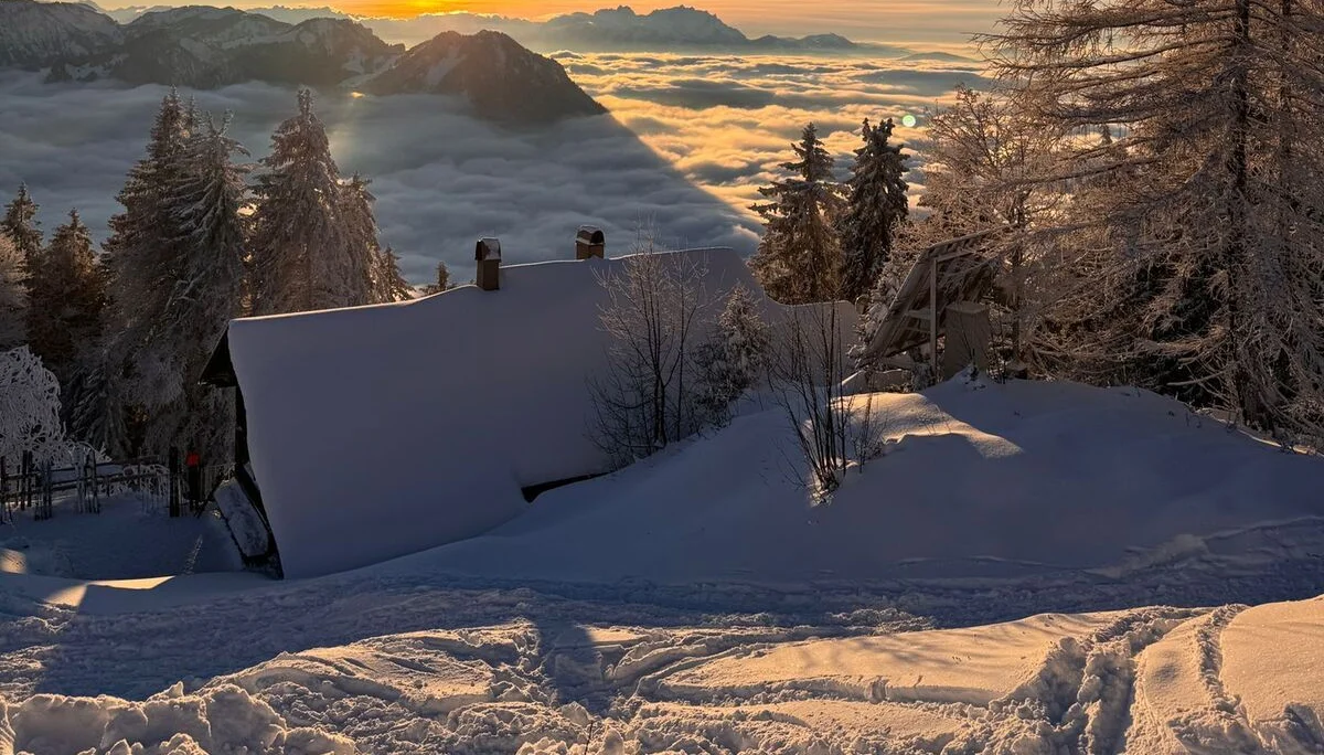 Schneebedecktes Hochälpele-Hütte vor verschneiten Bäumen und Bergen bei Sonnenuntergang über Wolkenmeer | © DAV-FN / Th. Gläser