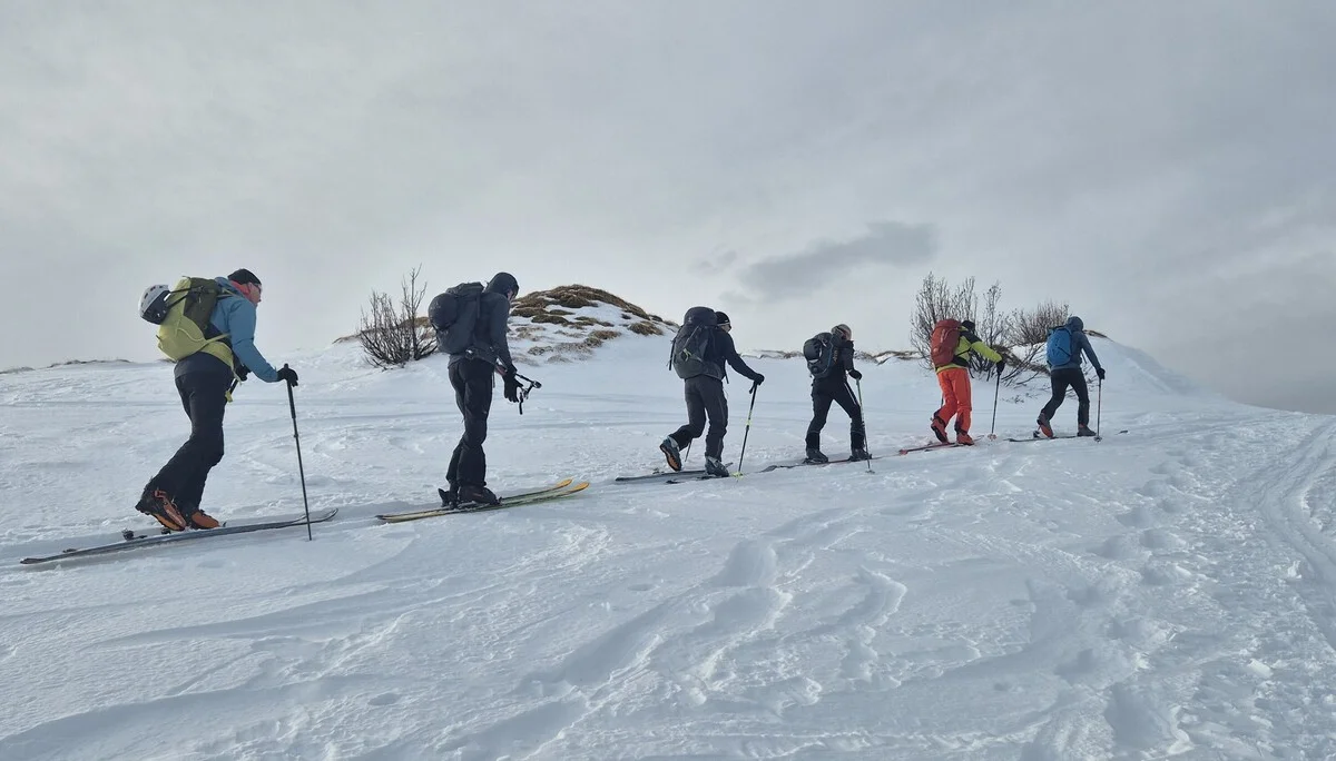 Fünf Skifahrer mit Rucksäcken steigen in einer Reihe einen schneebedeckten Hang hinauf | © DAV-Fn / R. Lebedeff