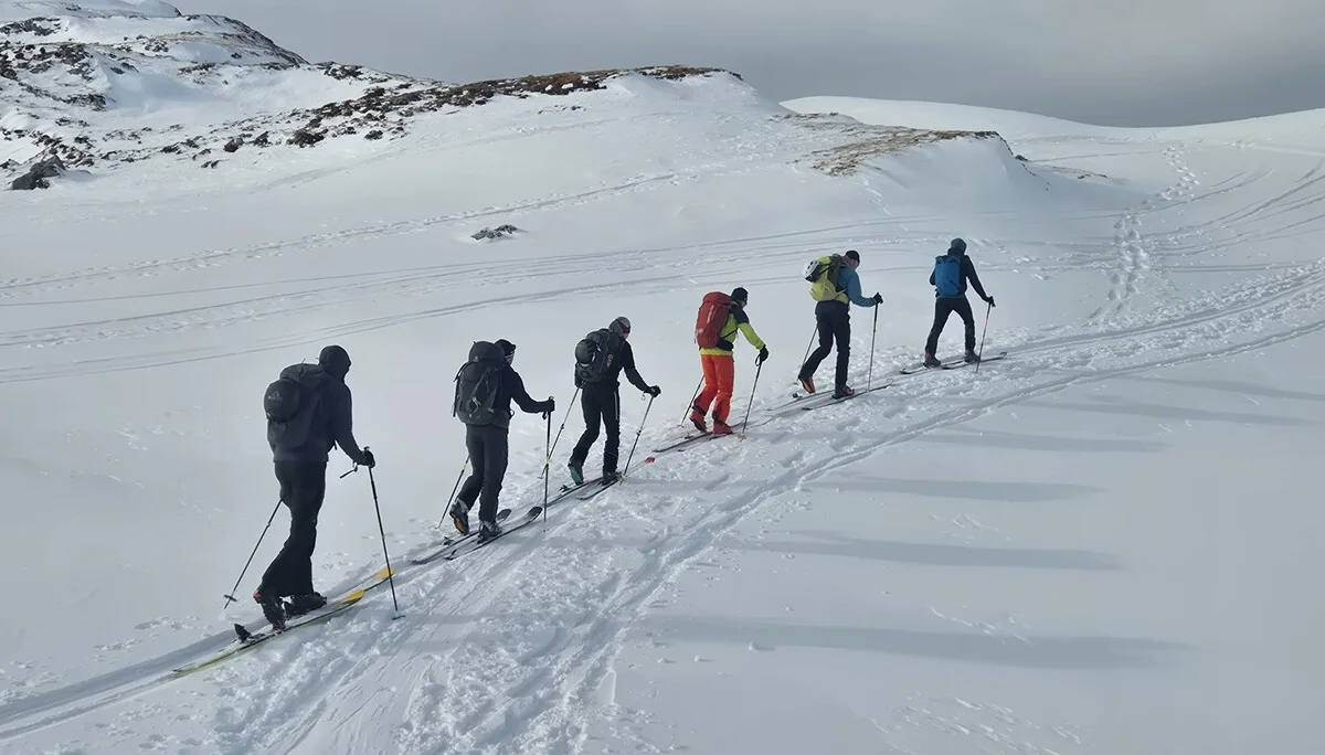 Sechs Skitourengeher in einer Reihe steigen auf verschneitem Berghang bei bewölktem Himmel auf | © DAV-Fn / R. Lebedeff