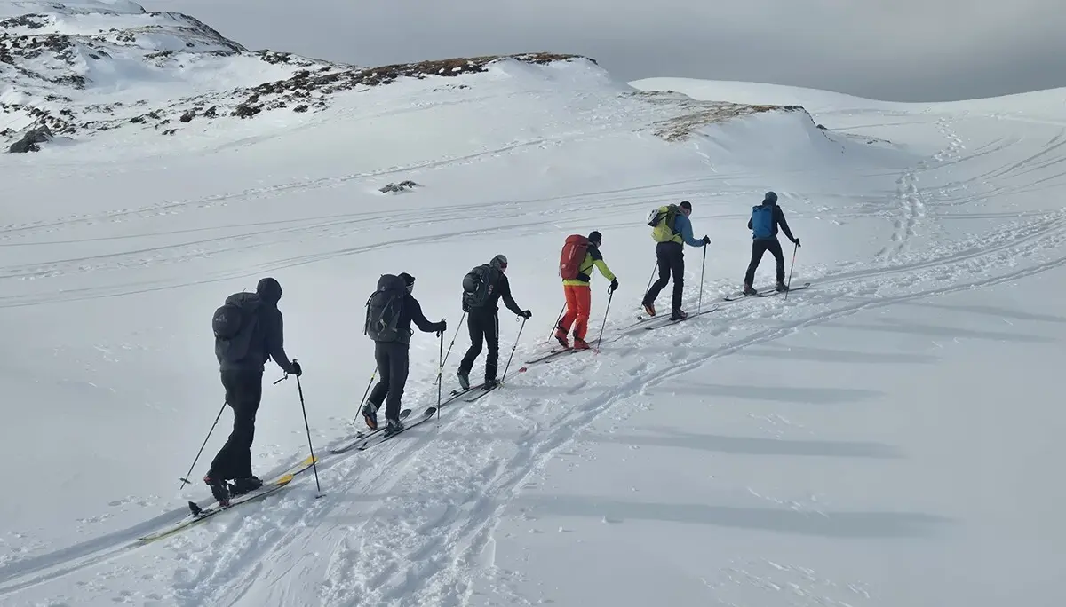 Sechs Skitourengeher in einer Reihe steigen auf verschneitem Berghang bei bewölktem Himmel auf | © DAV-Fn / R. Lebedeff