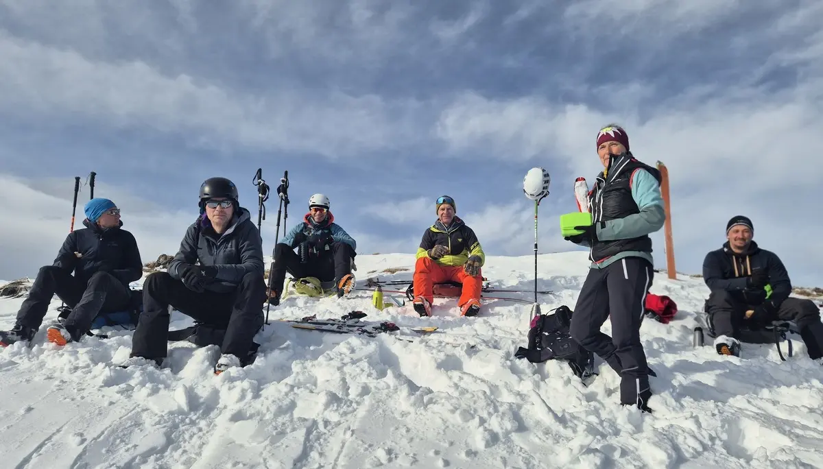 Gruppe von sechs Personen in Winterkleidung sitzt und steht auf schneebedecktem Hang unter bewölktem Himmel | © DAV-Fn / R. Lebedeff