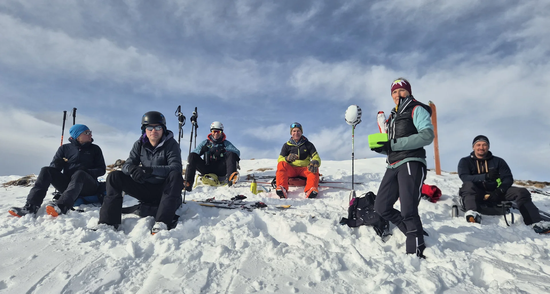 Gruppe von sechs Personen in Winterkleidung sitzt und steht auf schneebedecktem Hang unter bewölktem Himmel | © DAV-Fn / R. Lebedeff